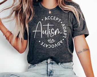 May include: A dark gray t-shirt with a white circle graphic that says "Accept, Autism, Adapt, Advocate" with two small hearts in the center.
