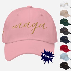 May include: A pink baseball cap with the word "maga" embroidered in gold script. The cap is available in nine colors.
