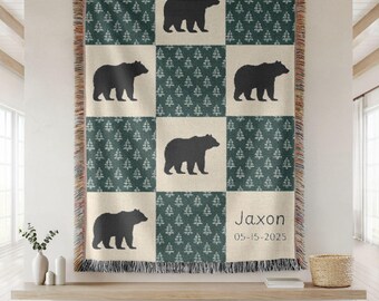 May include: A woven throw blanket with a patchwork design featuring black bear silhouettes and green tree patterns on a cream background. The blanket has a fringed edge and includes the name "Jaxon" and the date "05-15-2025".