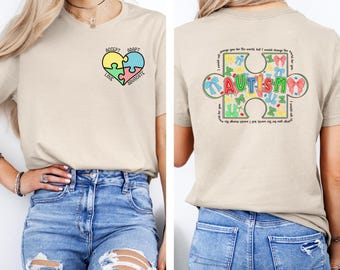 May include: A beige t-shirt with a heart-shaped puzzle piece design on the front. The puzzle pieces are yellow, blue, green, and pink. The text on the front reads "Accept, Adapt, Love, Advocate". The back of the shirt has a large puzzle piece with the word "AUTISM" in the center. The puzzle piece is filled with colorful bows and the text "I would change the world but I would change the world for you".