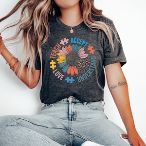 May include: A gray t-shirt with a colorful sunflower design. The sunflower is made up of puzzle pieces and the words "Teach, Love, Accept, Understand" are written around the sunflower.