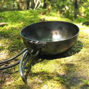 以下が含まれることがあります： 側面にハンドルが付いた黒い金属製のボウル。ボウルは緑の苔の上に置かれています。
