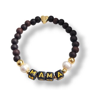 May include: A bracelet with dark brown and black wooden beads, gold accents, and the word "MAMA" spelled out in black and gold letter beads. A gold heart charm is also included.