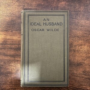 Könnte beinhalten: Ein grünes Buch mit schwarzem Rand und dem Titel "An Ideal Husband" von Oscar Wilde.
