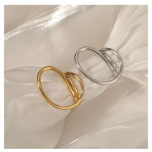 Puede incluir: Dos anillos con un diseño circular abierto y superpuesto. Un anillo tiene un acabado en tono dorado pulido y el otro en tono plateado pulido. El texto Scenarios, Selected high-qualitymaterials, not easy to allergies, The real gold pvd platingis not easy to fade es visible.