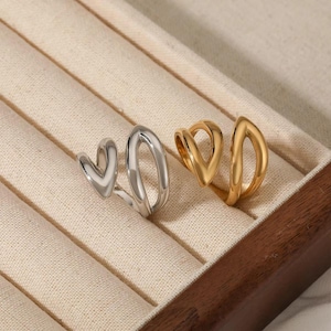 May include: Two open-style rings, one in a polished silver-tone finish and one in a polished gold-tone finish. Each ring features a smooth, continuous metal band that curves into a teardrop or V-shaped open design, creating a modern, sleek appearance.