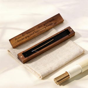 May include: A wooden incense holder with a burning incense stick inside. The rectangular box has a dark wood finish and a black felt interior. The lid is open, revealing the text "Burn the incense, calm your soul, Invite joy and harmony home."