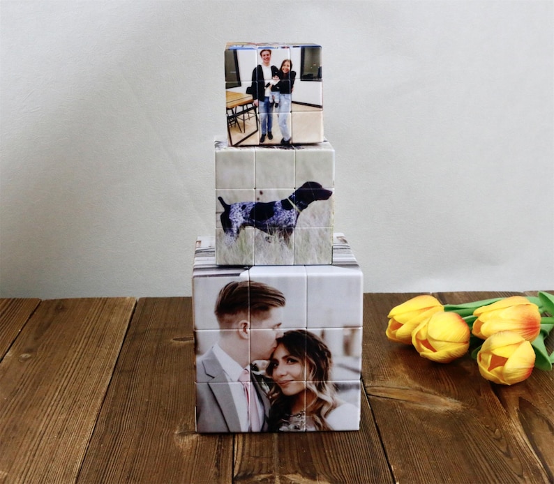 May include: Three personalized photo cubes stacked on a wooden surface. The cubes display images of a couple, a dog, and another couple. Yellow tulips are in the background.