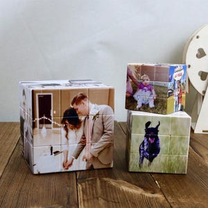 Op de afbeelding: Drie gepersonaliseerde fotoblokken, elk met verschillende afbeeldingen. Eén blok toont een trouwfoto, een ander een baby en de derde een hond. De blokken staan op een houten oppervlak, met een decoratief houten wiel op de achtergrond.