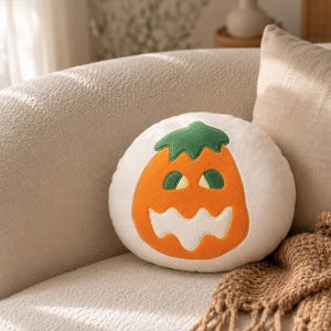 Puede incluir: Un coj&iacute;n redondo blanco con un dise&ntilde;o de calabaza naranja y verde para Halloween. El coj&iacute;n est&aacute; sobre un sof&aacute; beige con una manta marr&oacute;n. Perfecto para la decoraci&oacute;n de oto&ntilde;o y Halloween.