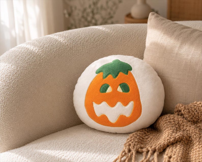 Puede incluir: Un coj&iacute;n redondo blanco con un dise&ntilde;o de calabaza naranja y verde para Halloween. El coj&iacute;n est&aacute; sobre un sof&aacute; beige con una manta marr&oacute;n. Perfecto para la decoraci&oacute;n de oto&ntilde;o y Halloween.