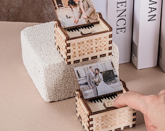 Könnte beinhalten: Zwei hölzerne Spieluhren mit Fotos eines Paares. Die Boxen haben ein Klaviertasten-Design und dekorative Muster. Eine Box ist geöffnet und zeigt das Foto und die Tasten. Die andere Box ist geschlossen.