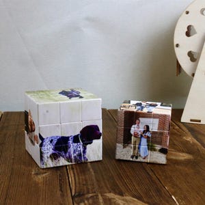 May include: Two photo cubes with images of a dog and a couple. The dog cube features a German Shorthaired Pointer. The other cube displays a couple in front of a brick building. A wooden heart-shaped decoration is in the background.