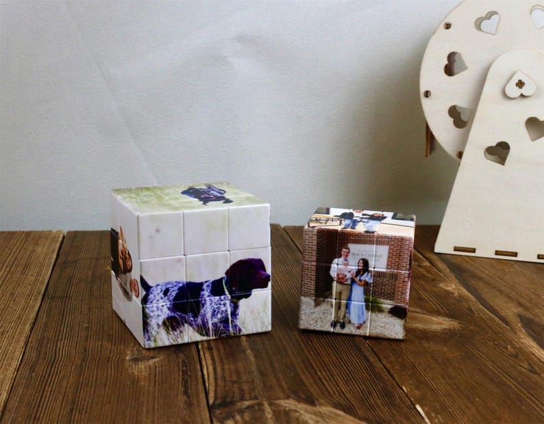 May include: Two photo cubes with images of a dog and a couple. The dog cube features a German Shorthaired Pointer. The other cube displays a couple in front of a brick building. A wooden heart-shaped decoration is in the background.