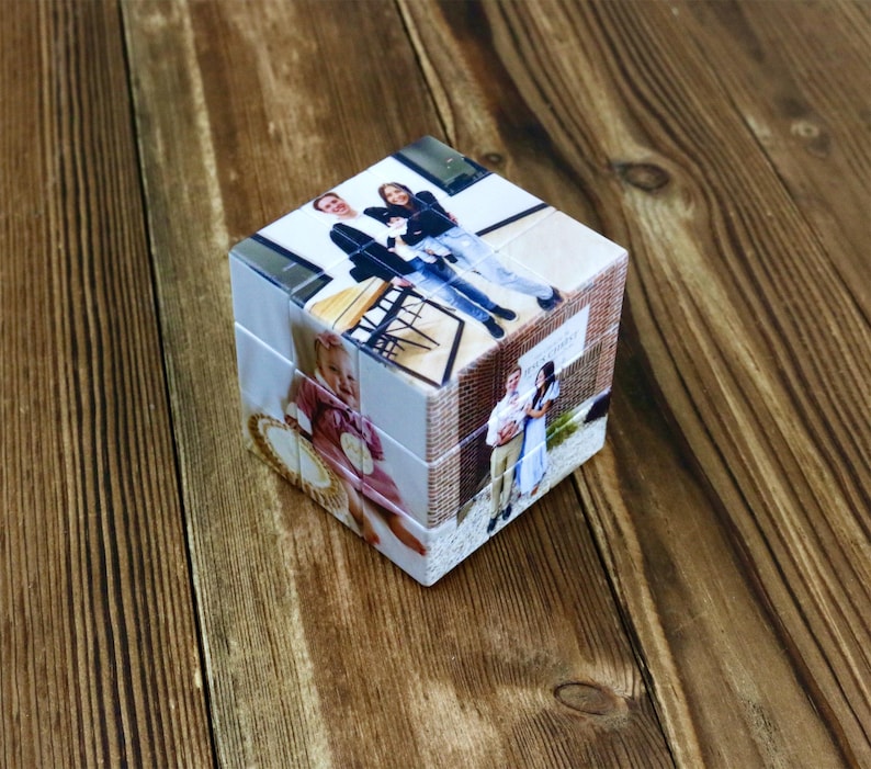 May include: A personalized photo cube puzzle with images of people and brick wall patterns. The cube sits on a wooden surface, showcasing the custom printed photos on each side. A unique gift idea.