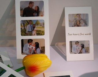 May include: Two white picture frames with photos of couples and a baby. The frames have the text "Two hearts, one world" written on them. A yellow tulip is in the foreground.