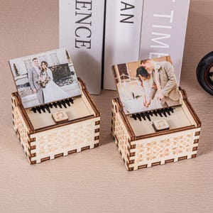 Op de afbeelding: Twee houten muziekdozen met een trouwfoto. De dozen hebben een pianotoetsontwerp en een muzieknoot. Ze zijn gemaakt van lichtbruin hout met decoratieve uitsparingen.