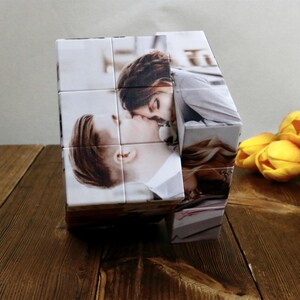 May include: A personalized photo cube featuring images of a couple kissing. The cube is made of white material and displays the photos on its sides. Yellow tulips are in the background.
