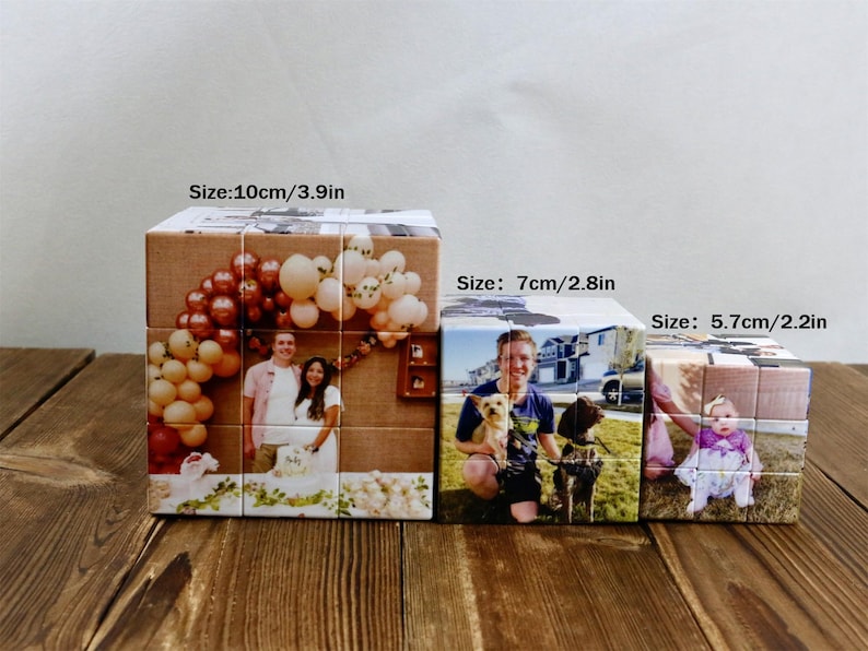 May include: Three personalized photo cubes of varying sizes (10cm/3.9in, 7cm/2.8in, and 5.7cm/2.2in) sit on a wooden surface. Each cube displays a different photograph, including a wedding photo, a person with dogs, and a baby.