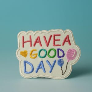 May include: White embroidered patch with the text "HAVE A GOOD DAY" in rainbow colors. Two small balloons are embroidered on the right side of the patch.