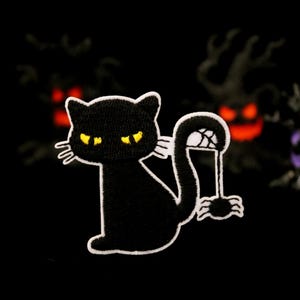 May include: Black cat patch with yellow eyes and white outline, holding a spider in its tail. The patch is set against a dark background with Halloween-themed decorations, including a skull.