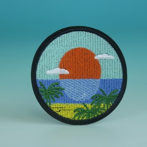 May include: A round embroidered patch with a sunset over the ocean scene. The patch features a bright orange sun, blue water, white clouds, and two green palm trees.