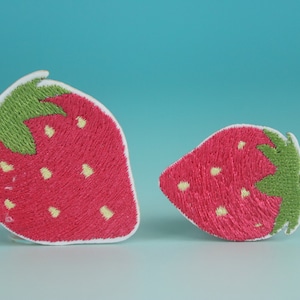 May include: Two embroidered strawberry patches, one larger than the other, with green leaves and white stitching on a light blue background.