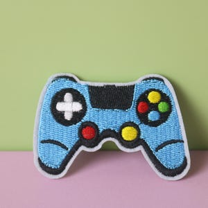 May include: A blue embroidered patch shaped like a video game controller with black, white, red, yellow, and green buttons.