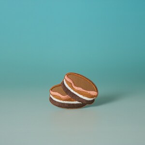 May include: Two brown and white cookies with pink frosting stacked on top of each other against a light blue background.