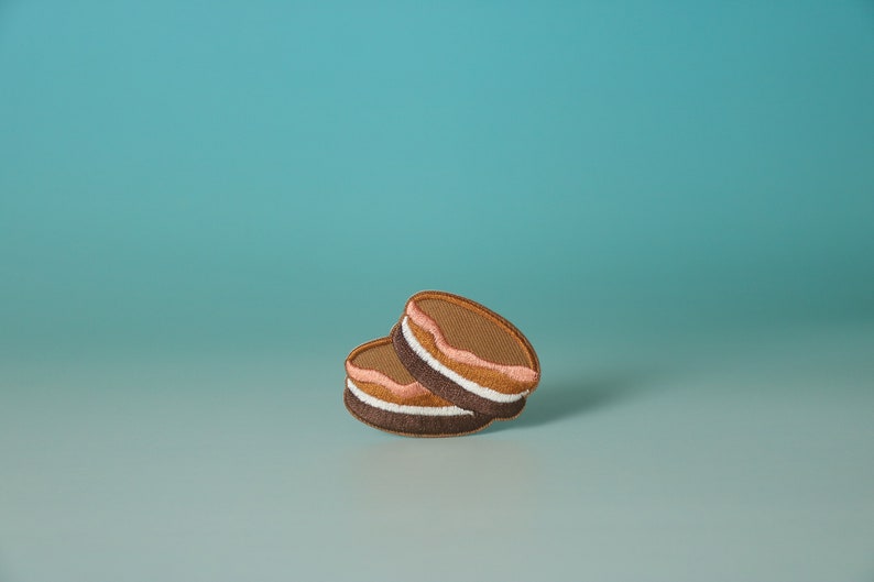May include: Two brown and white cookies with pink frosting stacked on top of each other against a light blue background.