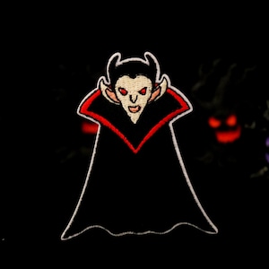 Puede incluir: Un parche bordado que representa a un vampiro con colmillos y una capa. El vampiro es negro y rojo con una cara blanca y ojos rojos.
