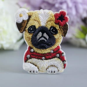 May include: Embroidered iron-on patch of a pug wearing a red sweater with white polka dots and a white flower and red flower on its head.