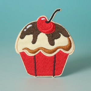 May include: A red, white, and brown embroidered cupcake patch with a cherry on top. The cupcake has chocolate icing.