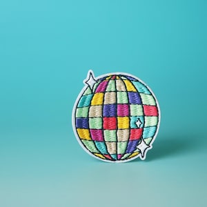 Könnte beinhalten: Ein bunter gestickter Aufnäher mit einer Discokugel und weißen Sternen. Die Discokugel besteht aus Quadraten in verschiedenen Farben, darunter Rot, Gelb, Grün, Blau und Lila.
