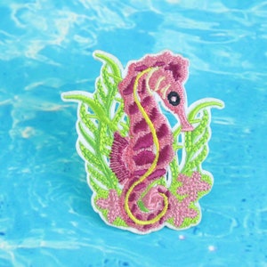 Peut inclure: Hippocampe brodé rose et jaune avec des algues vertes, sur un fond bleu.