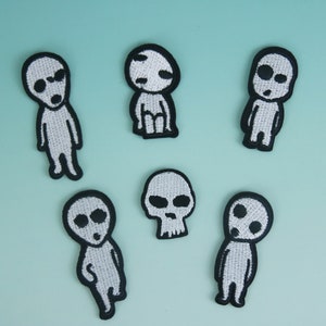 May include: Six white embroidered patches on a light blue background. The patches are of various characters, including a skull and a few humanoid figures with large eyes.