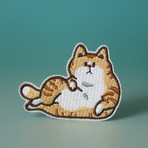Può includere: Toppa ricamata da stirare con un gatto dei cartoni animati sdraiato su un fianco con le zampe in aria. Il gatto è arancione e bianco con strisce marroni.