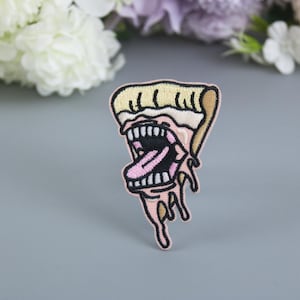 May include: A pink and yellow embroidered iron-on patch of a pizza slice with a cartoon mouth and tongue sticking out.