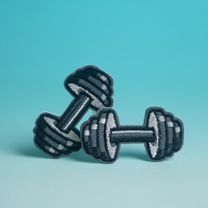 May include: Two embroidered dumbbell patches in grey and white, set against a light blue background. The patches have a textured appearance, suggesting a fabric or thread construction. The dumbbells are a symbol of fitness and exercise.