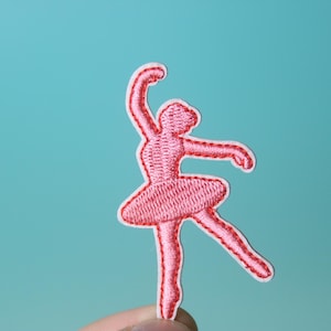 Puede incluir: Parche de bailarina bordada de color rosa sobre fondo blanco.
