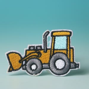 May include: A yellow embroidered iron-on patch of a cartoon bulldozer with black outlines and a light blue window.
