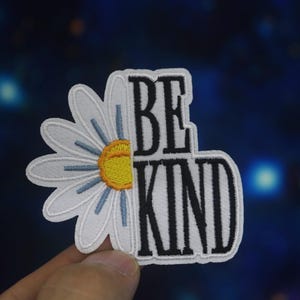 May include: White embroidered patch with a daisy and the words "Be Kind" in black.