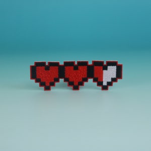 May include: A pixelated heart health bar with three red hearts, one of which is half-filled with white.