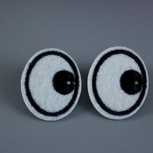 Puede incluir: Dos ojos saltones de fieltro blanco con pupilas negras y contornos negros.