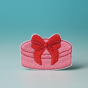 May include: A pink embroidered patch shaped like a gift box with a red bow on top.