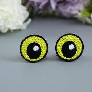Puede incluir: Dos parches para ojos bordados de color amarillo con pupilas negras y reflejos blancos.