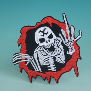 May include: A white skeleton with a red, dripping border, giving the middle finger. The skeleton is wearing a black shirt and has a skull with a white X on its forehead.