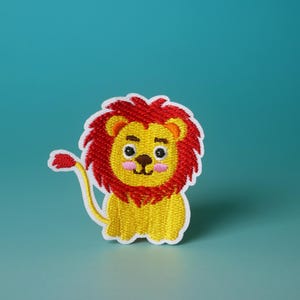 May include: A yellow lion with a red mane and a white outline. The lion has a cute, cartoon-like face with black eyes and pink cheeks.
