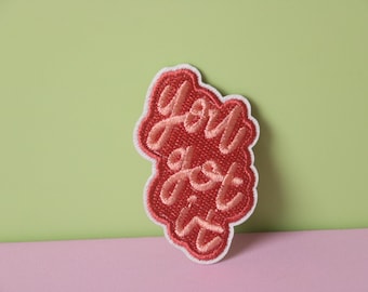 Könnte beinhalten: Ein rosa gestickter Aufnäher mit dem Text "You got it" in einem weißen Umriss.