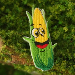 Peut inclure: Un patch brod&eacute; repr&eacute;sentant un &eacute;pi de ma&iuml;s avec un visage souriant. L'&eacute;pi de ma&iuml;s est vert et jaune avec un contour blanc et est entour&eacute; de feuilles vertes.